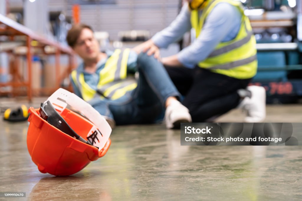 Selective focus at hat, Men worker feel painful and hurt from the accident that happen inside of industrial factory while his co-worker come to give emergency assistance and help. Accident in factory.